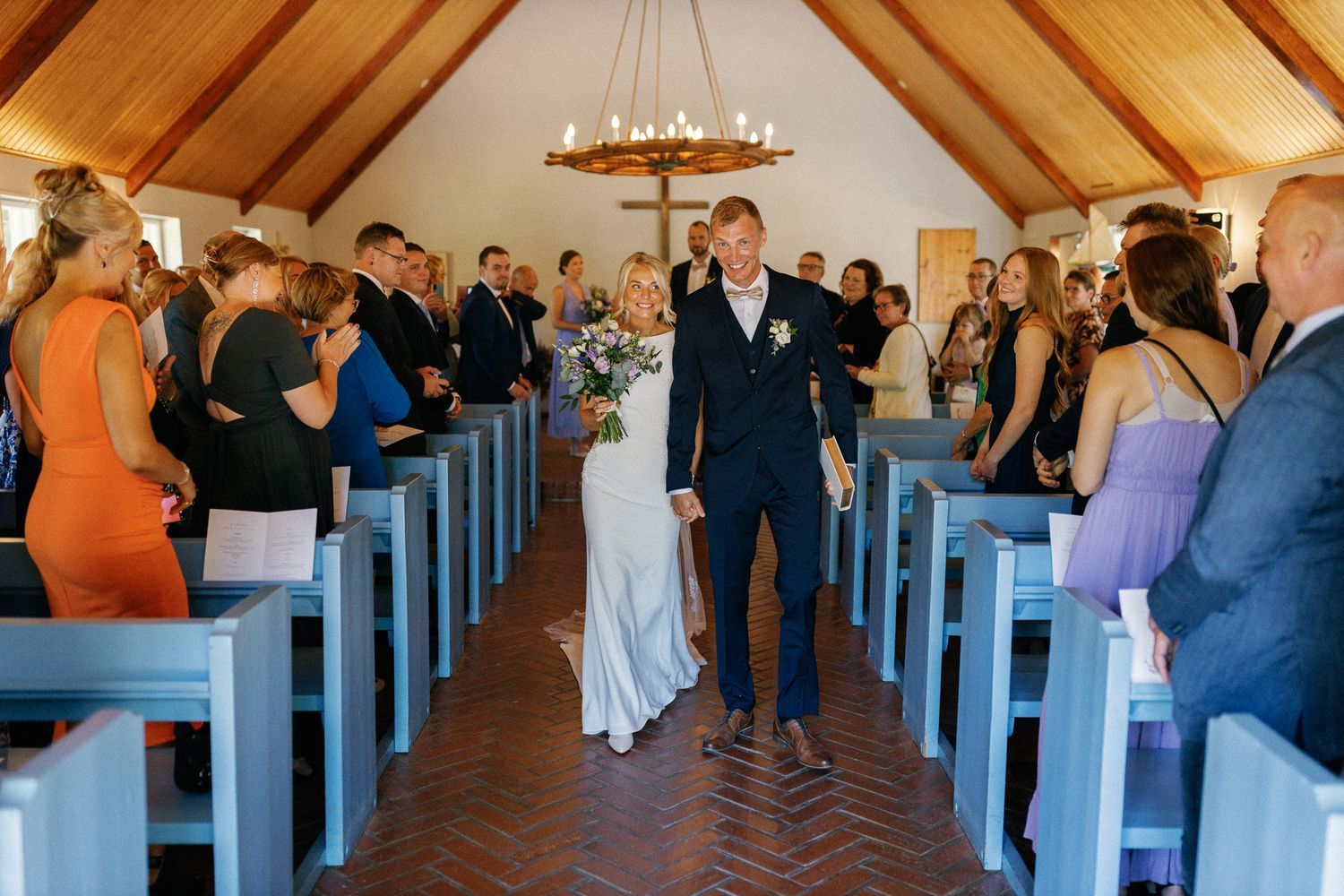 Guests fill the blue pews of a rustic chapel during a wedding ceremony.