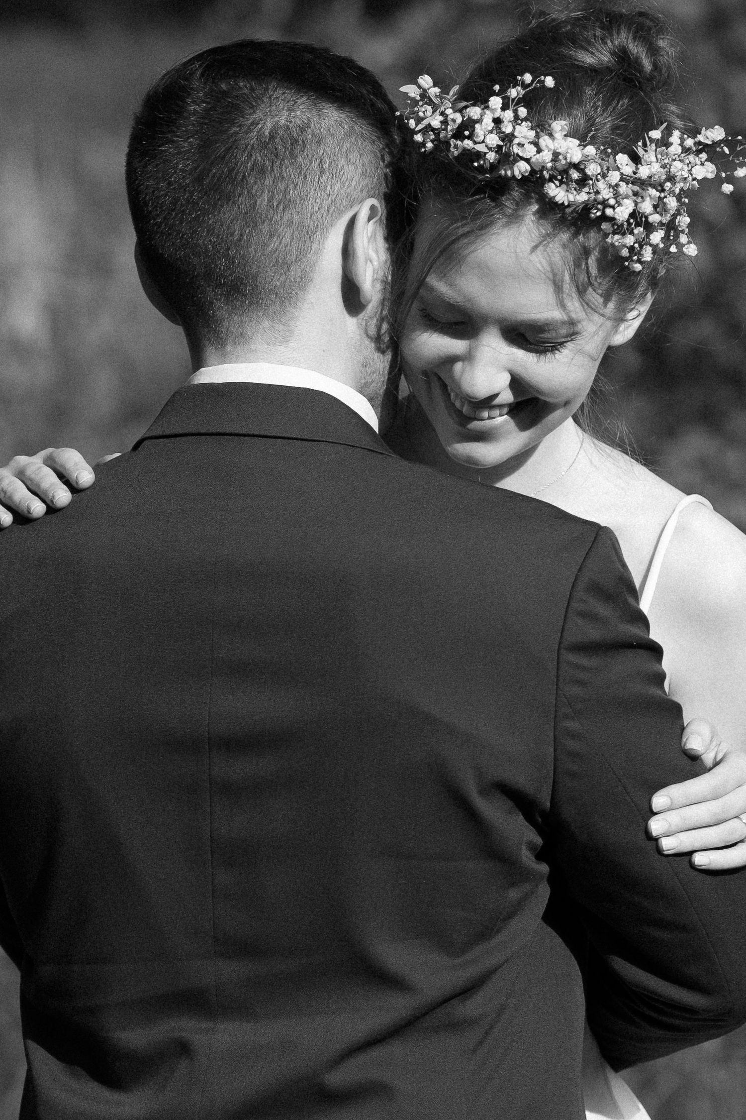 A romantic black and white portrait of newlyweds embracing, with the bride wearing a delicate floral crown.