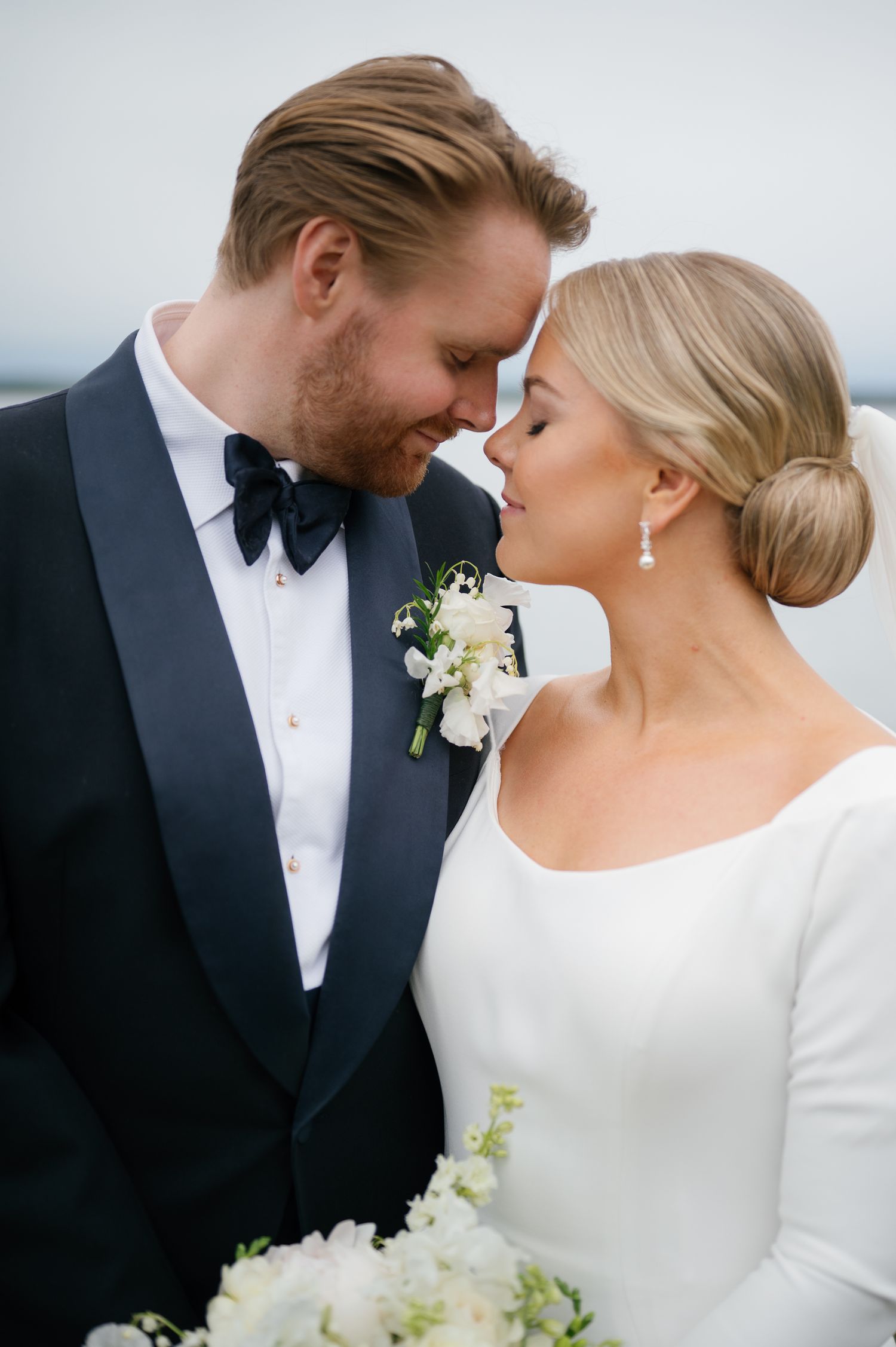 Elegant bride and groom share intimate moments in formal black and white wedding attire with delicate floral bouquet details.