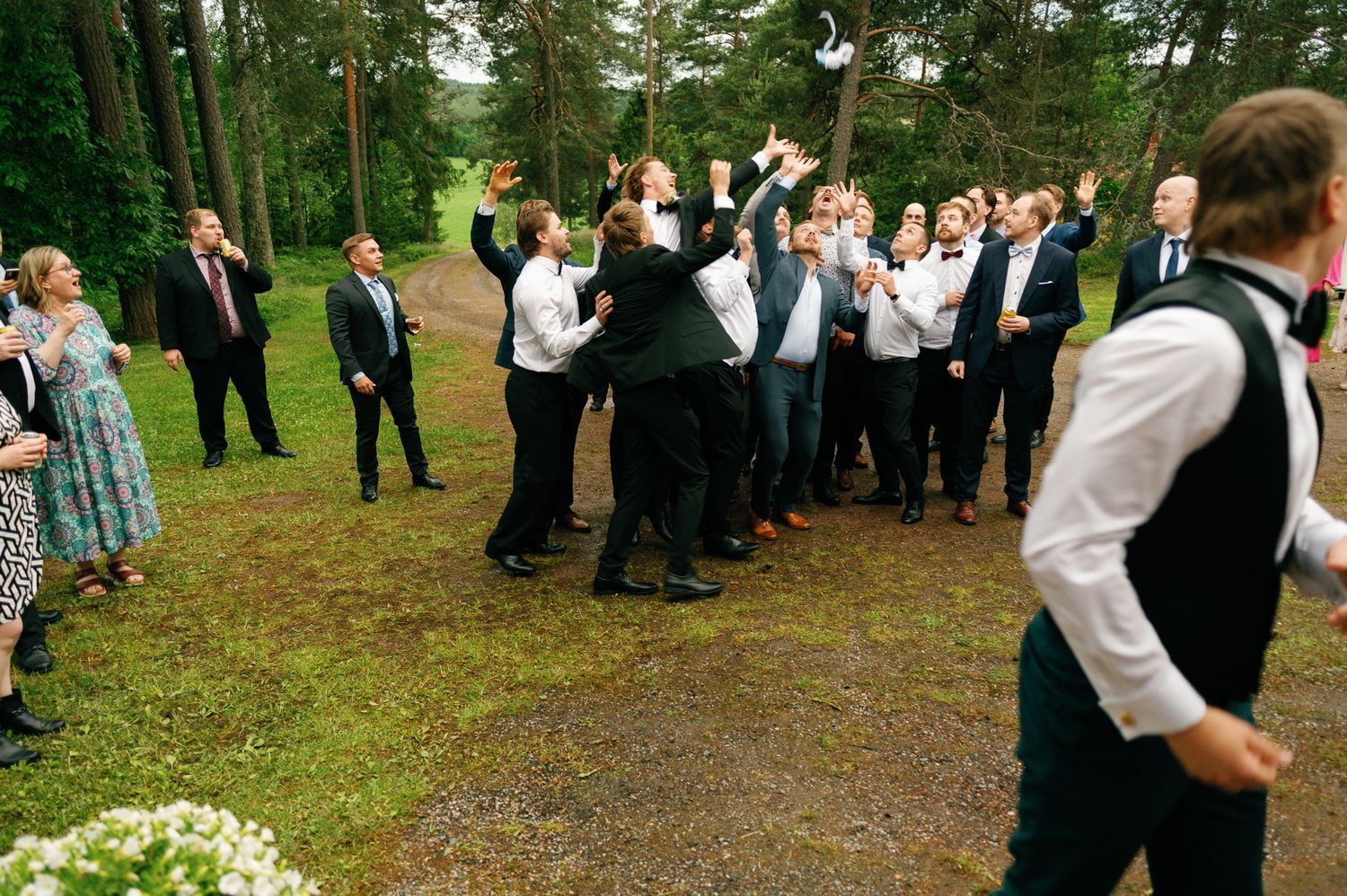 Wedding guests lined up outdoors among pine trees for a group activity.