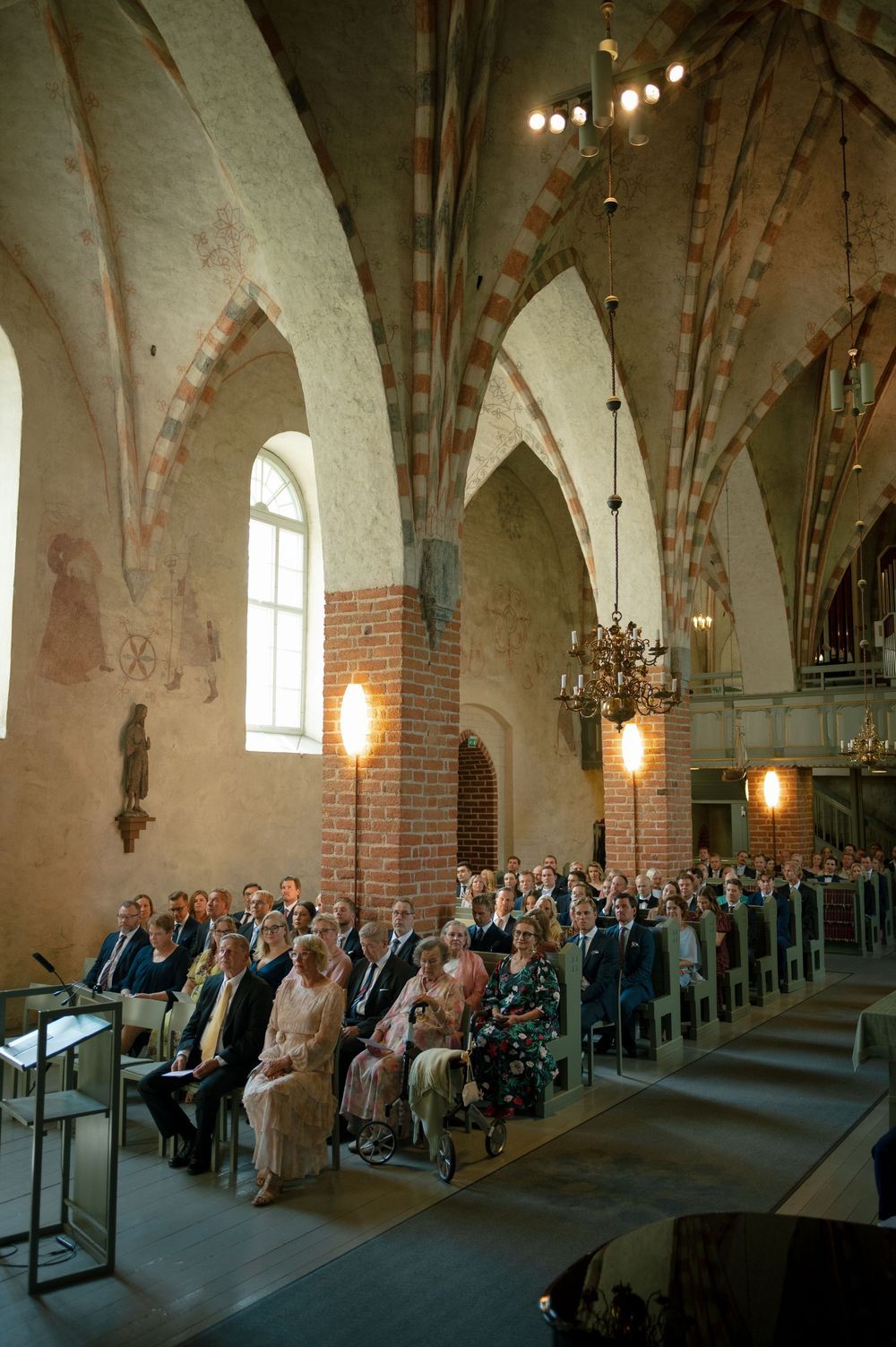 Interior of medieval-style church with vaulted ceilings and brick arches filled with wedding guests.