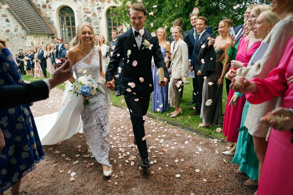 Colorful wedding celebration with guests tossing confetti outside stone church.