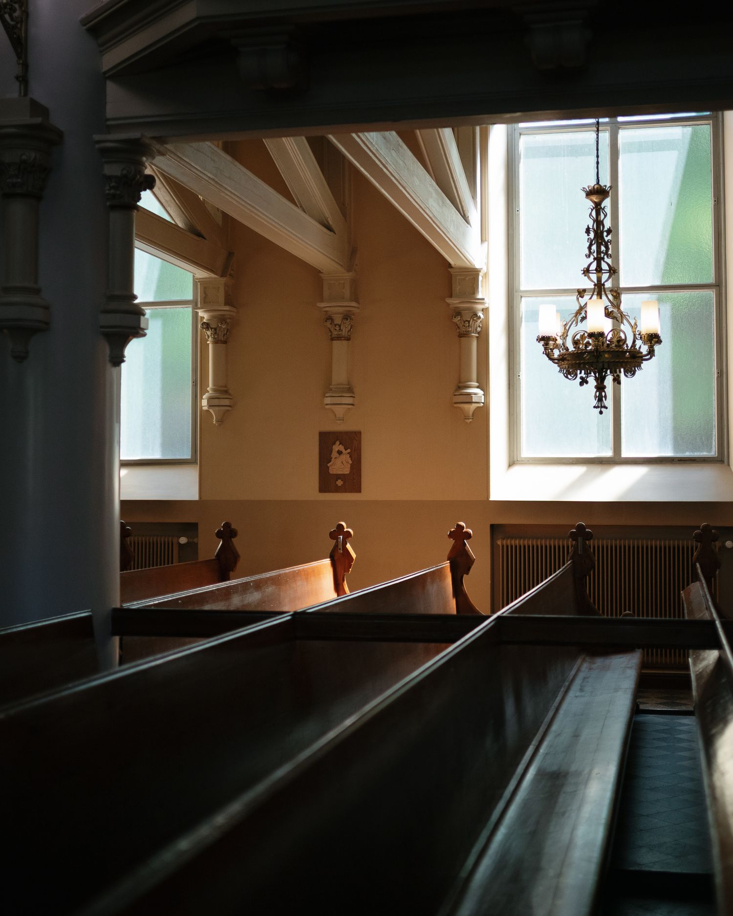 Sunlit church interior with wooden pews, ornate chandelier, white columns, and warm amber walls bathed in natural window light.