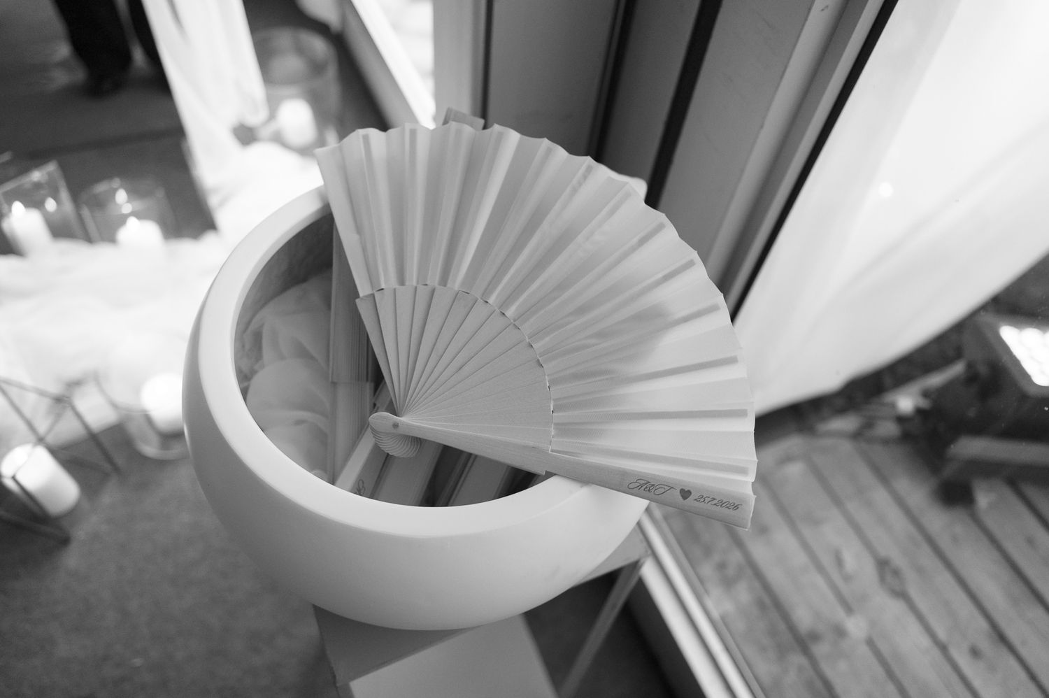 Black and white photo of a decorative hand fan resting on a spiral staircase near a window.