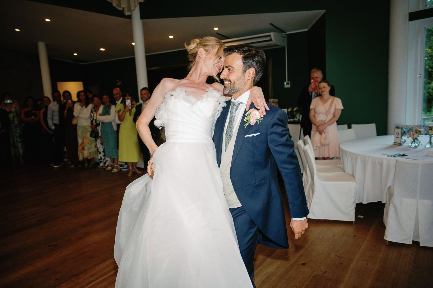 Newlyweds share romantic moment on dance floor, bride in white gown and groom in navy suit.