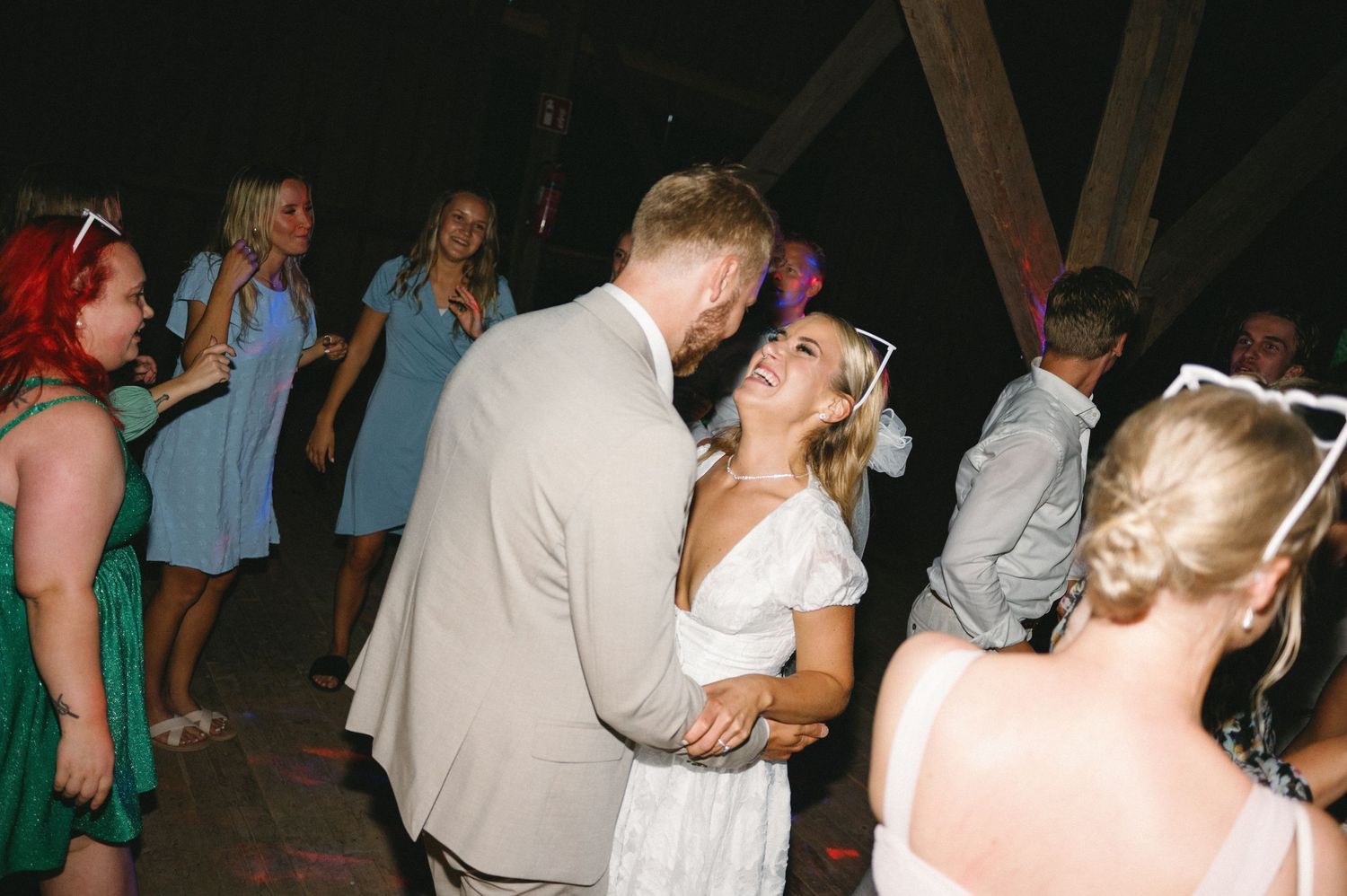 Wedding guests dancing and mingling at evening reception under warm lighting.