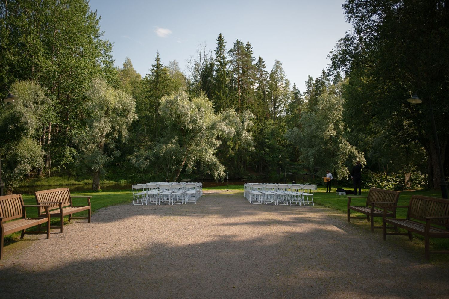 Panoramic view of a tree-lined park path with white structures in the background.