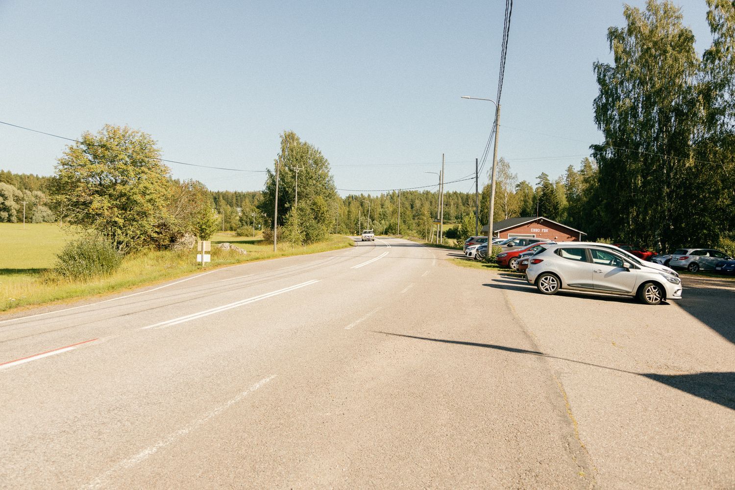 Empty rural road with trees and buildings in the distance.