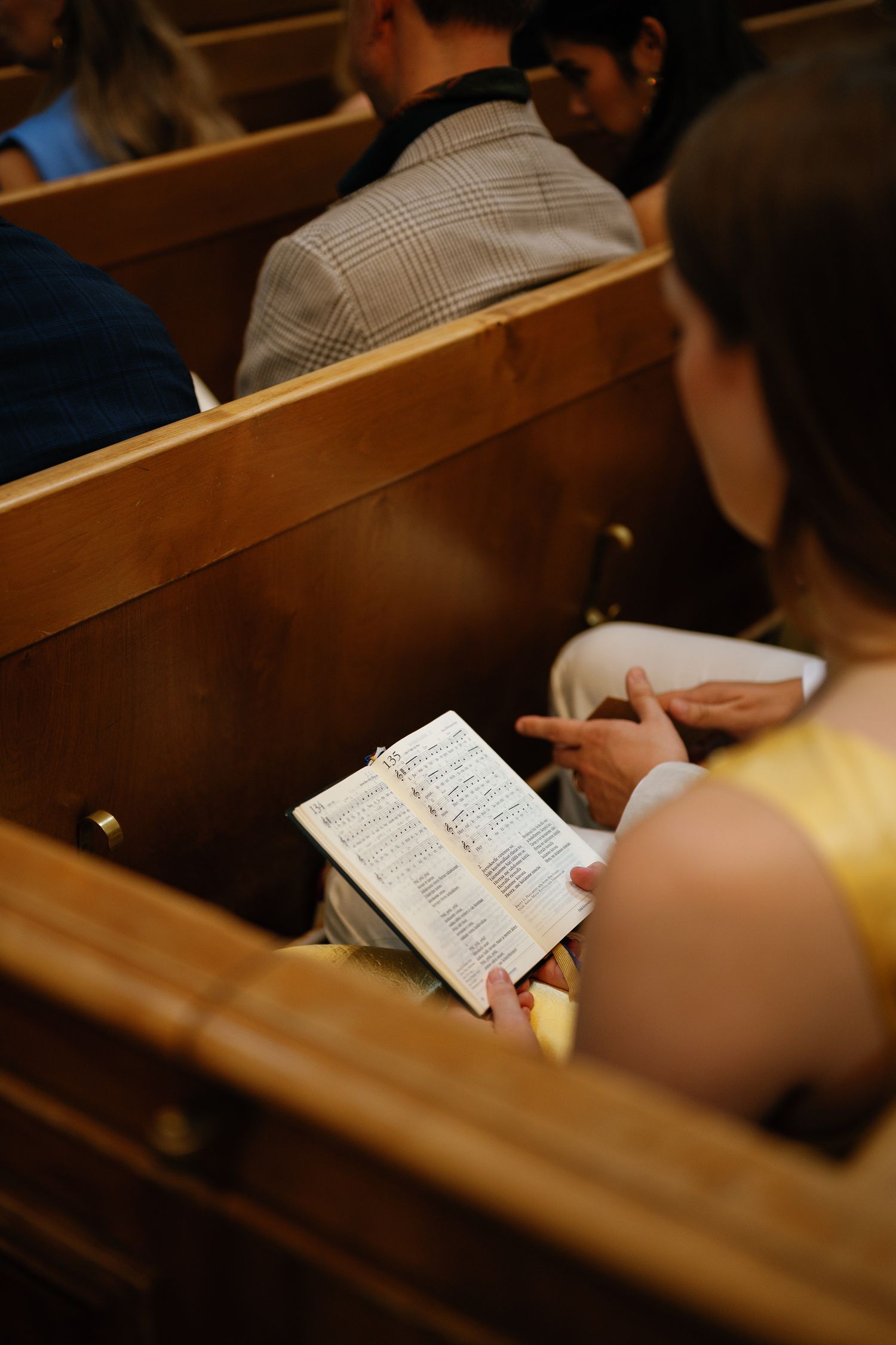 Woman in yellow top reading a program booklet while seated in wooden church pews during a service.