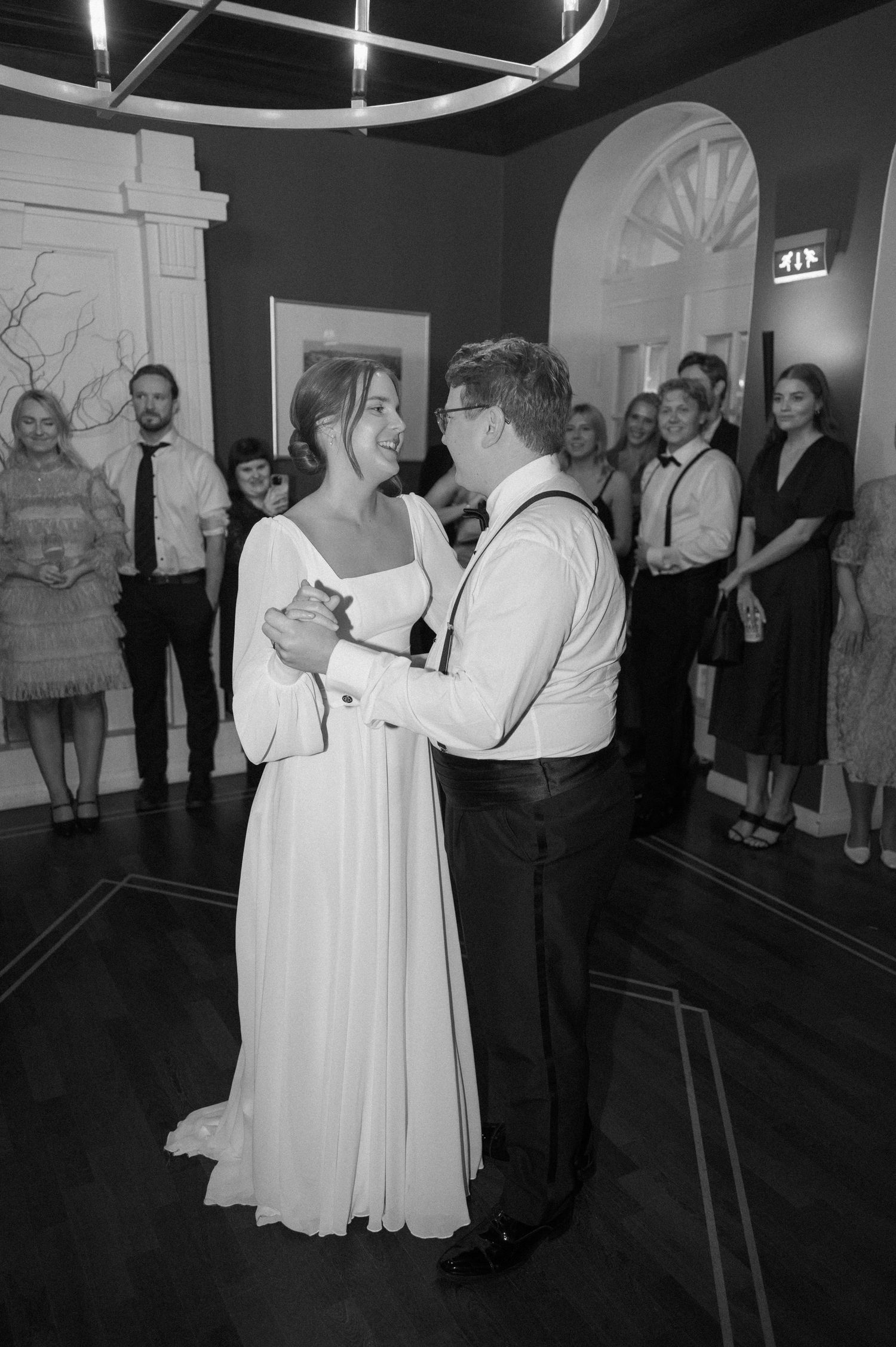 A couple shares their first dance at a wedding reception while guests watch from the edges of the dance floor.