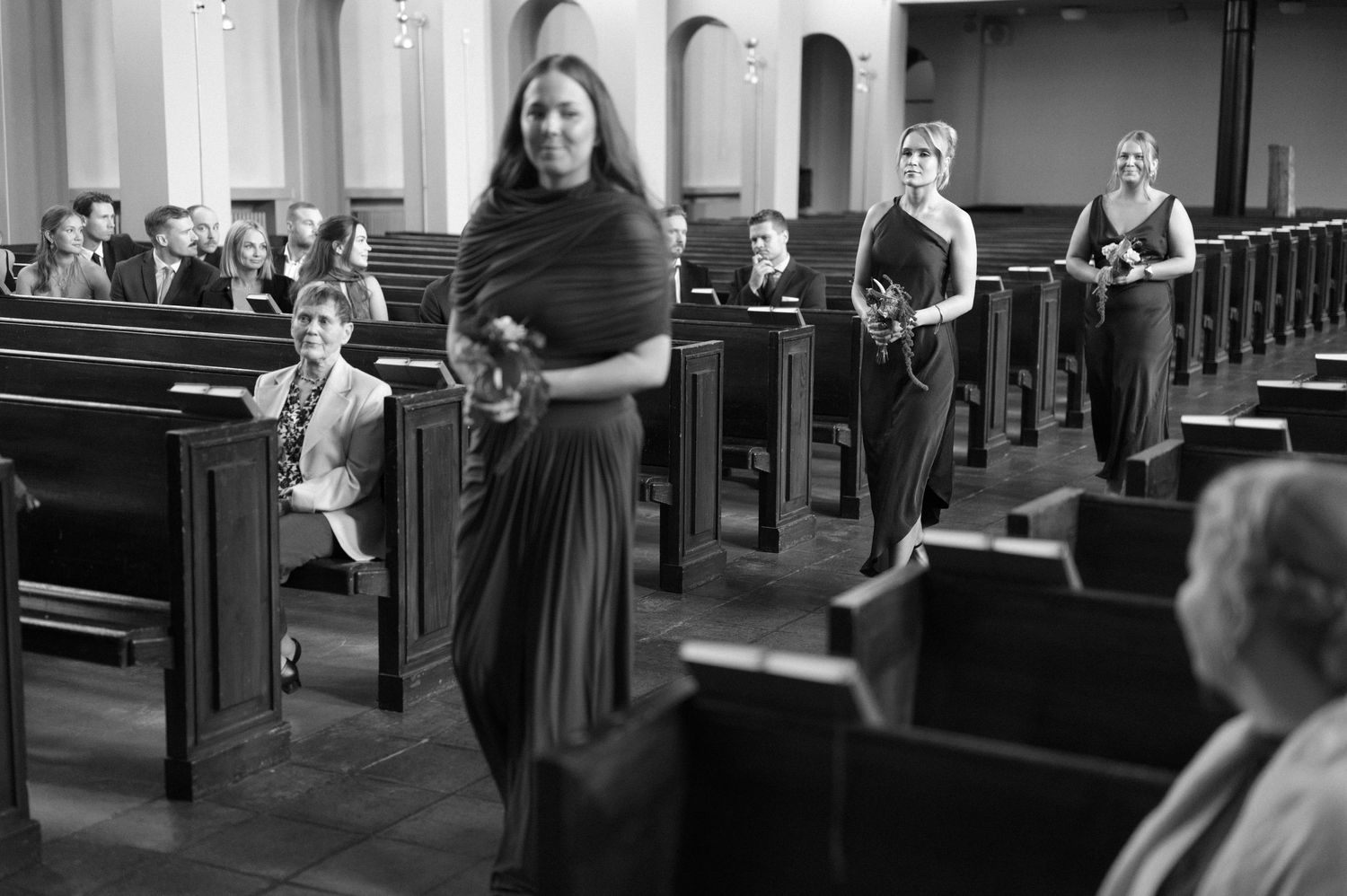 Black and white photo of people sitting in church pews during what appears to be a wedding ceremony.