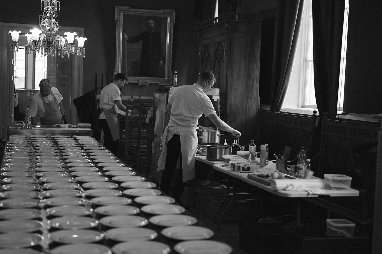 Black and white interior view of a formal dining room being prepared for service.