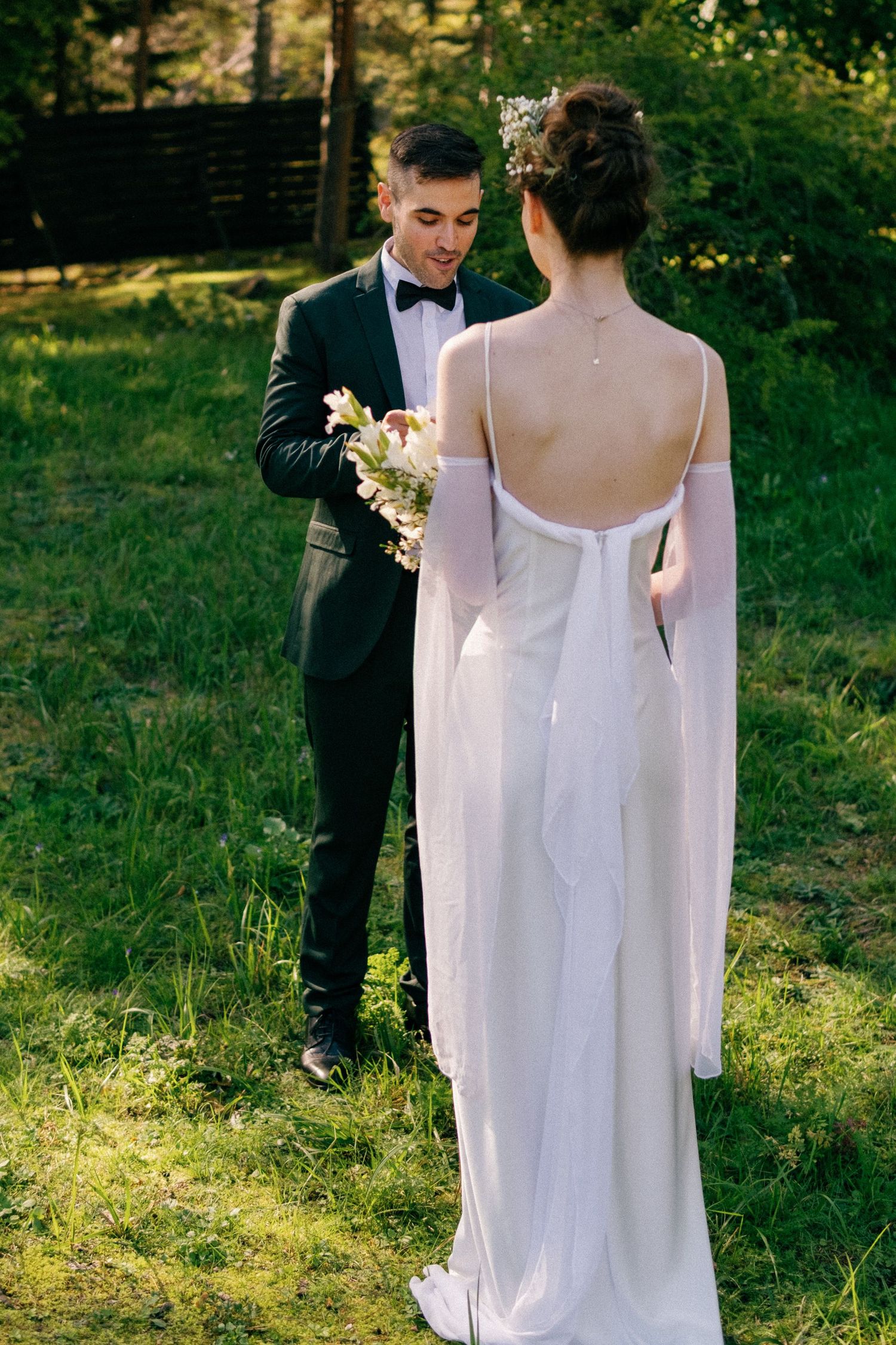 Elegant outdoor wedding scene with flowing white dress against lush green landscape.