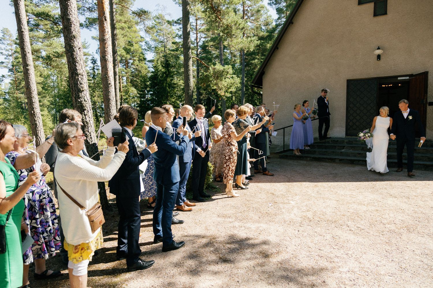 Guests gather outside a forest chapel for a summer wedding celebration.