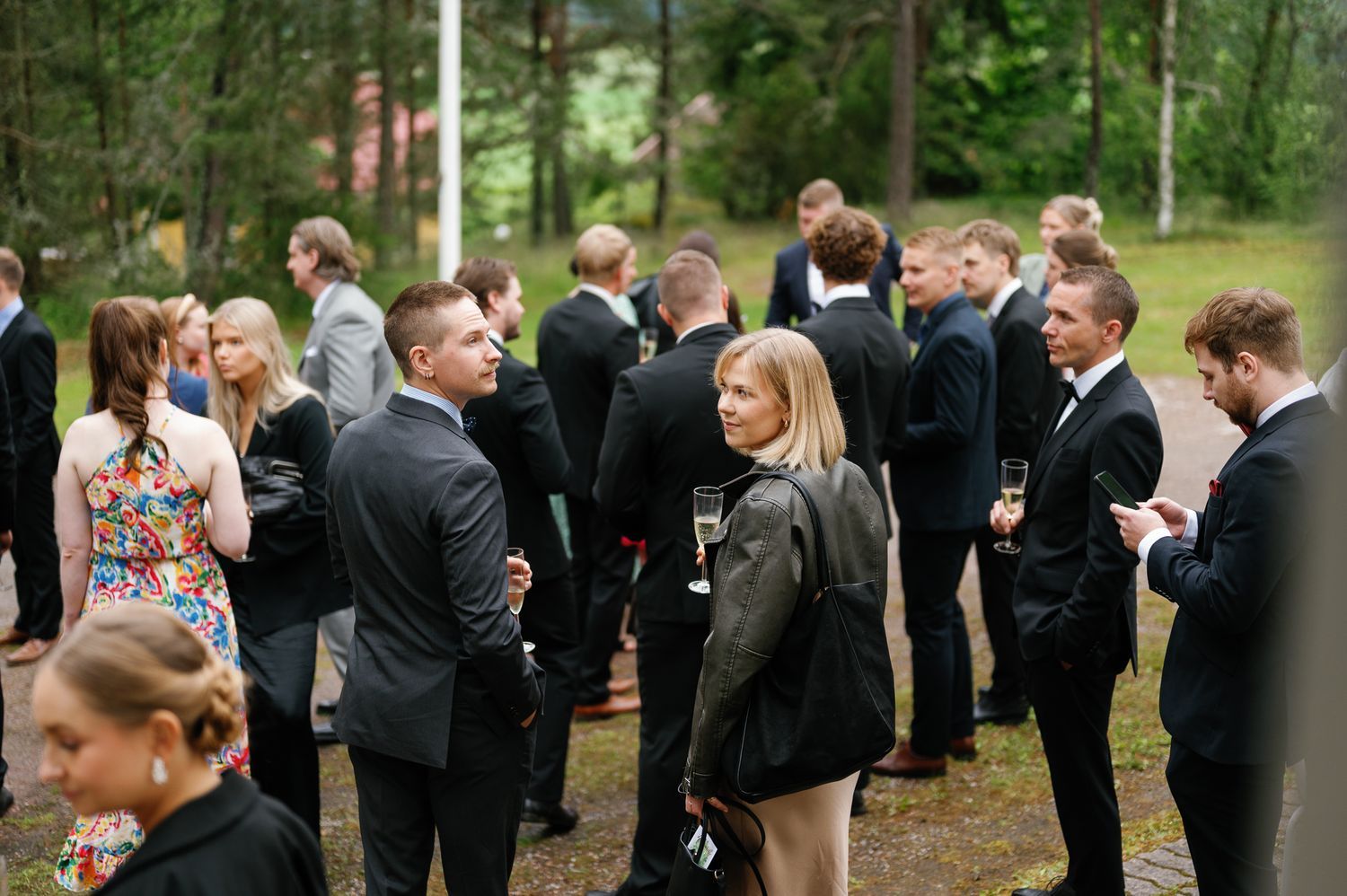 Wedding guests gathered outdoors in formal attire among trees.