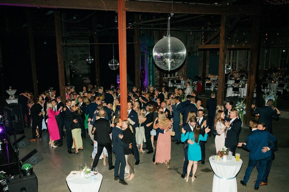 Wedding guests fill a converted warehouse space decorated with purple lighting and a disco ball.
