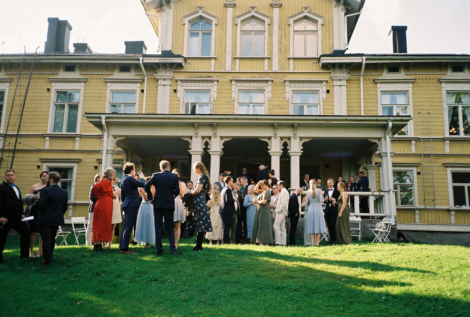 Wedding guests gathered on lawn in front of grand yellow mansion.