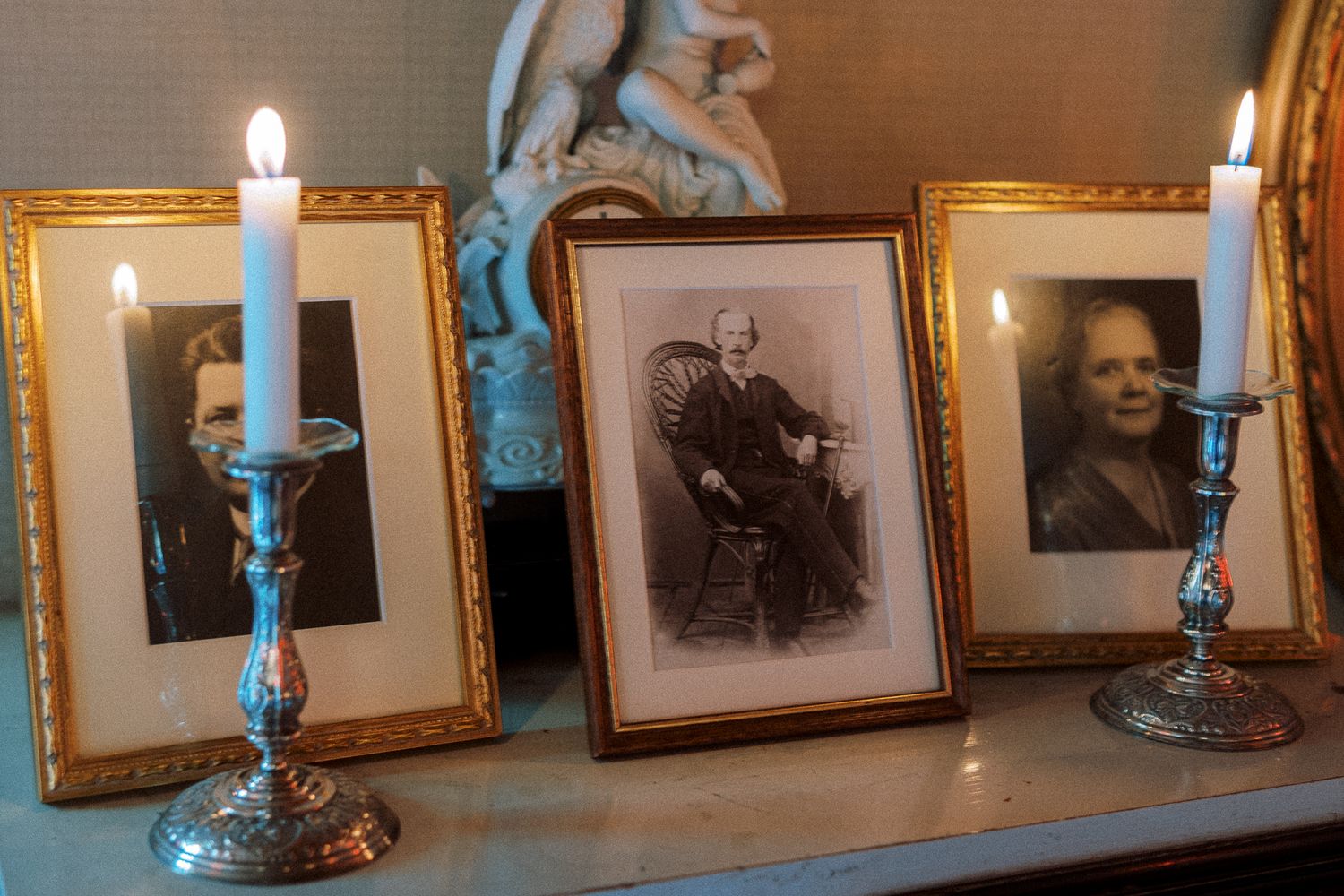 A vintage gallery wall with lit candles and framed photographs displayed in ornate gold frames along a shelf.
