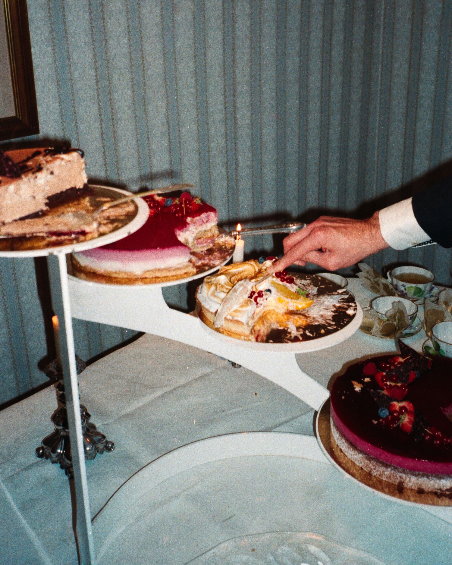 A dessert table spread featuring various cakes and pies on white plates and platters arranged in a buffet style setting.