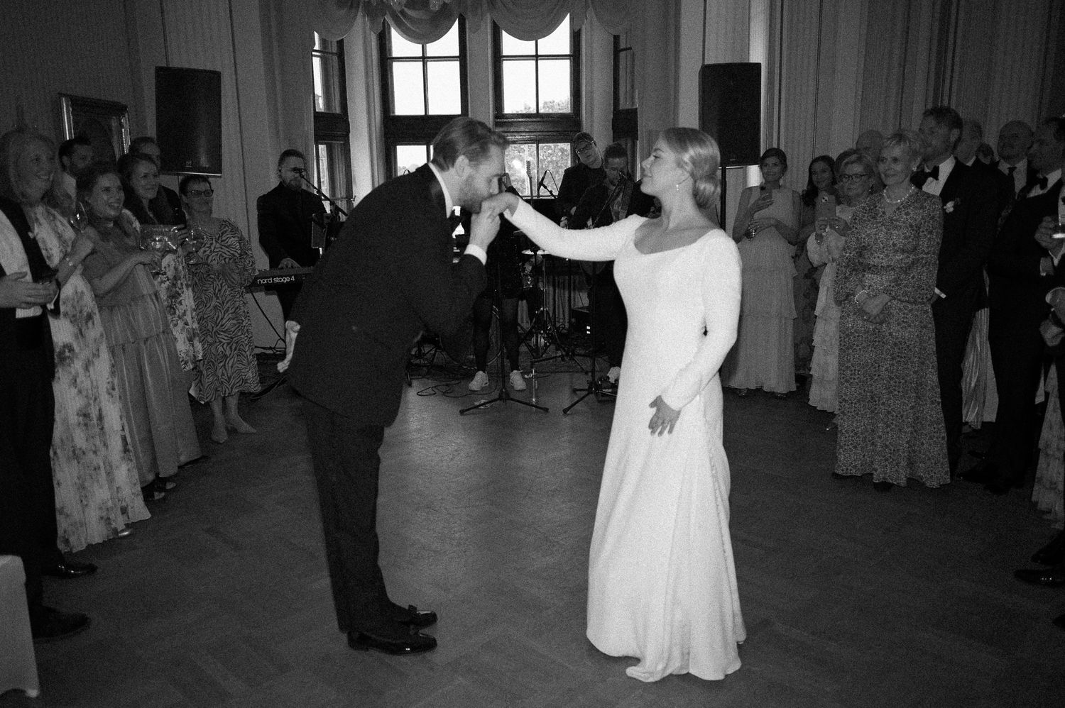 A couple shares their first dance at a wedding reception while guests look on in this black and white photograph.