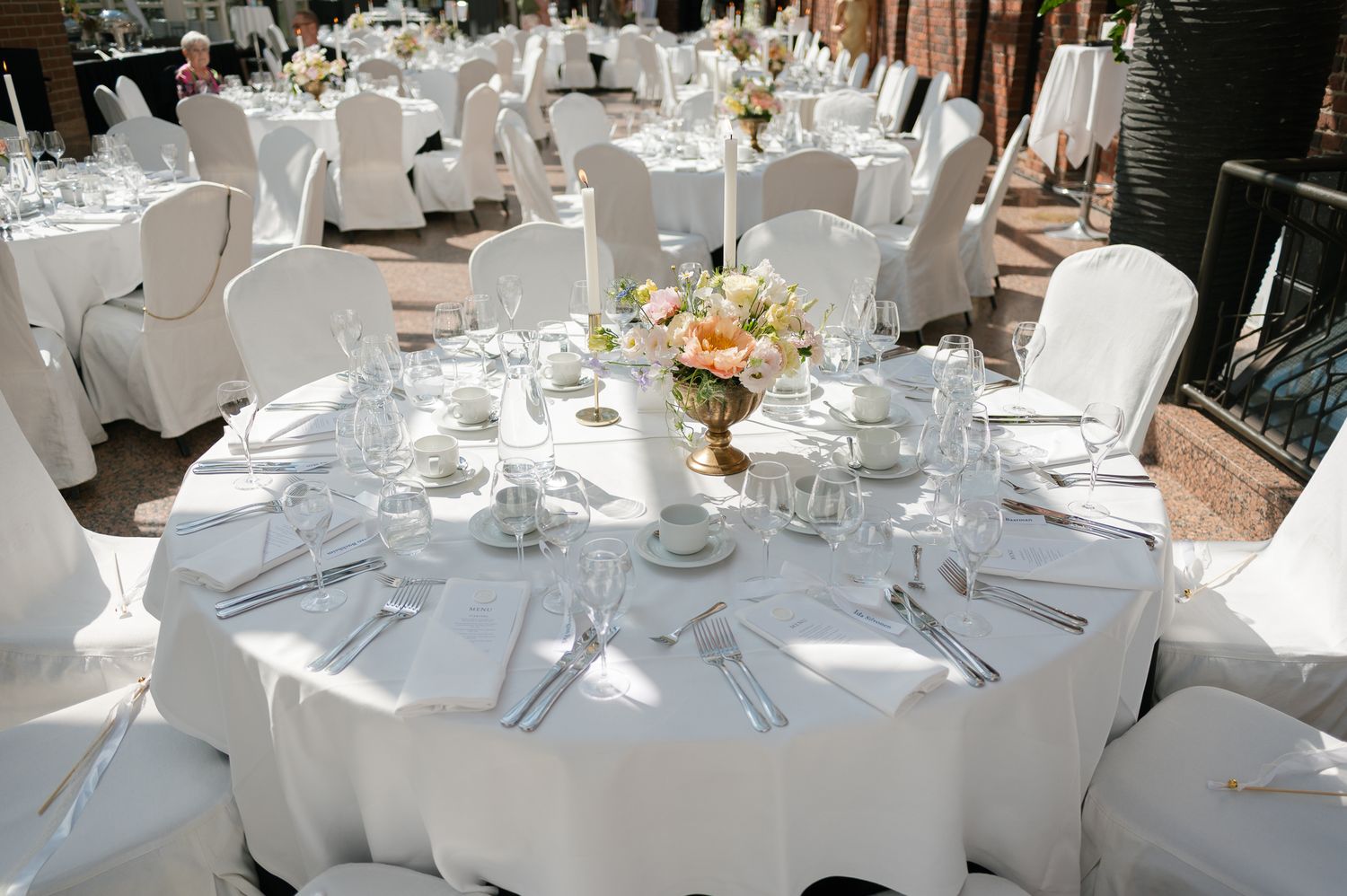 Elegant outdoor wedding reception with round tables draped in white linens, floral centerpieces, and white chair covers.