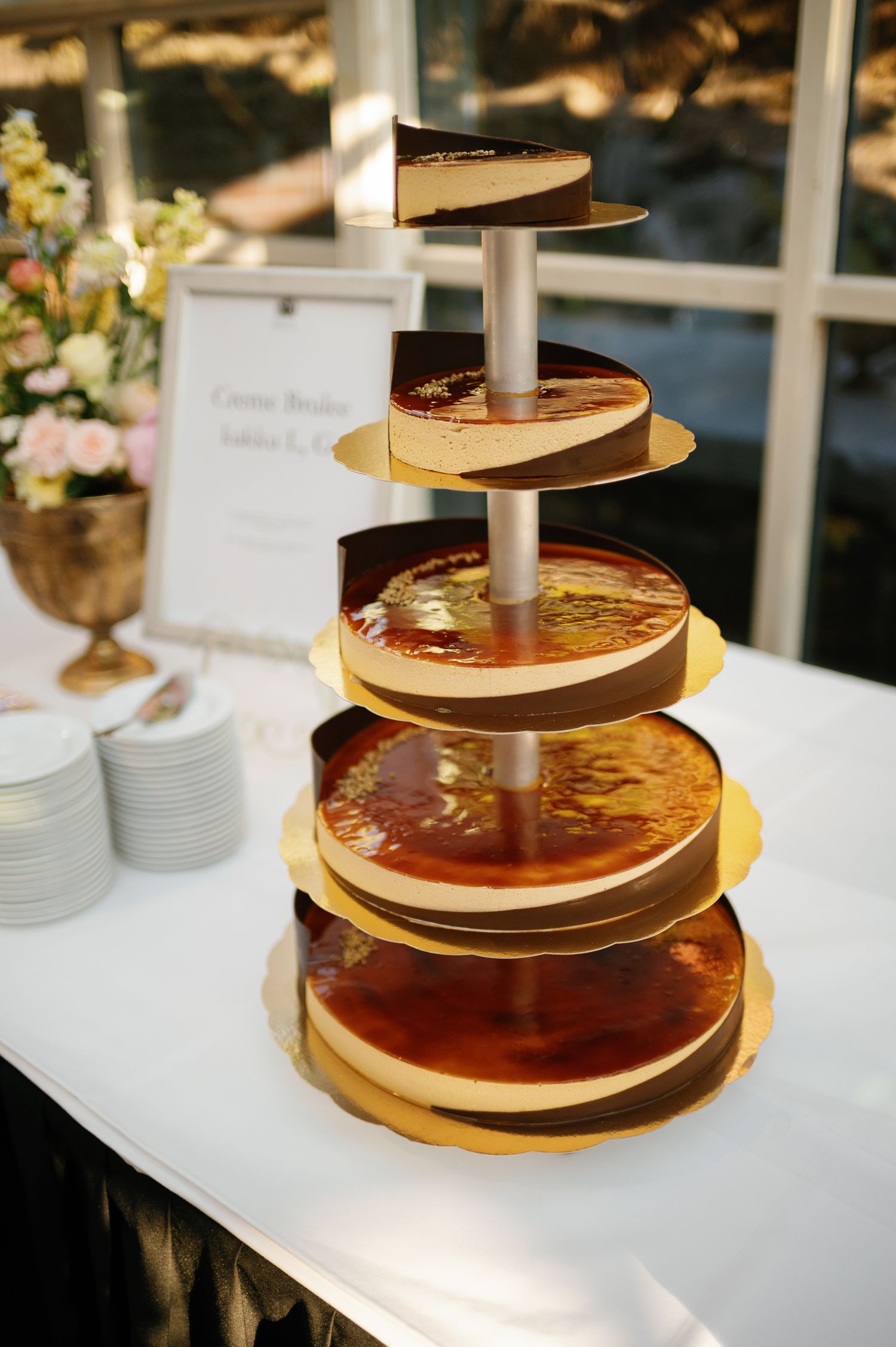 Elegant five-tier cheesecake tower with caramel glaze on gold boards displayed on a white table at a wedding reception.