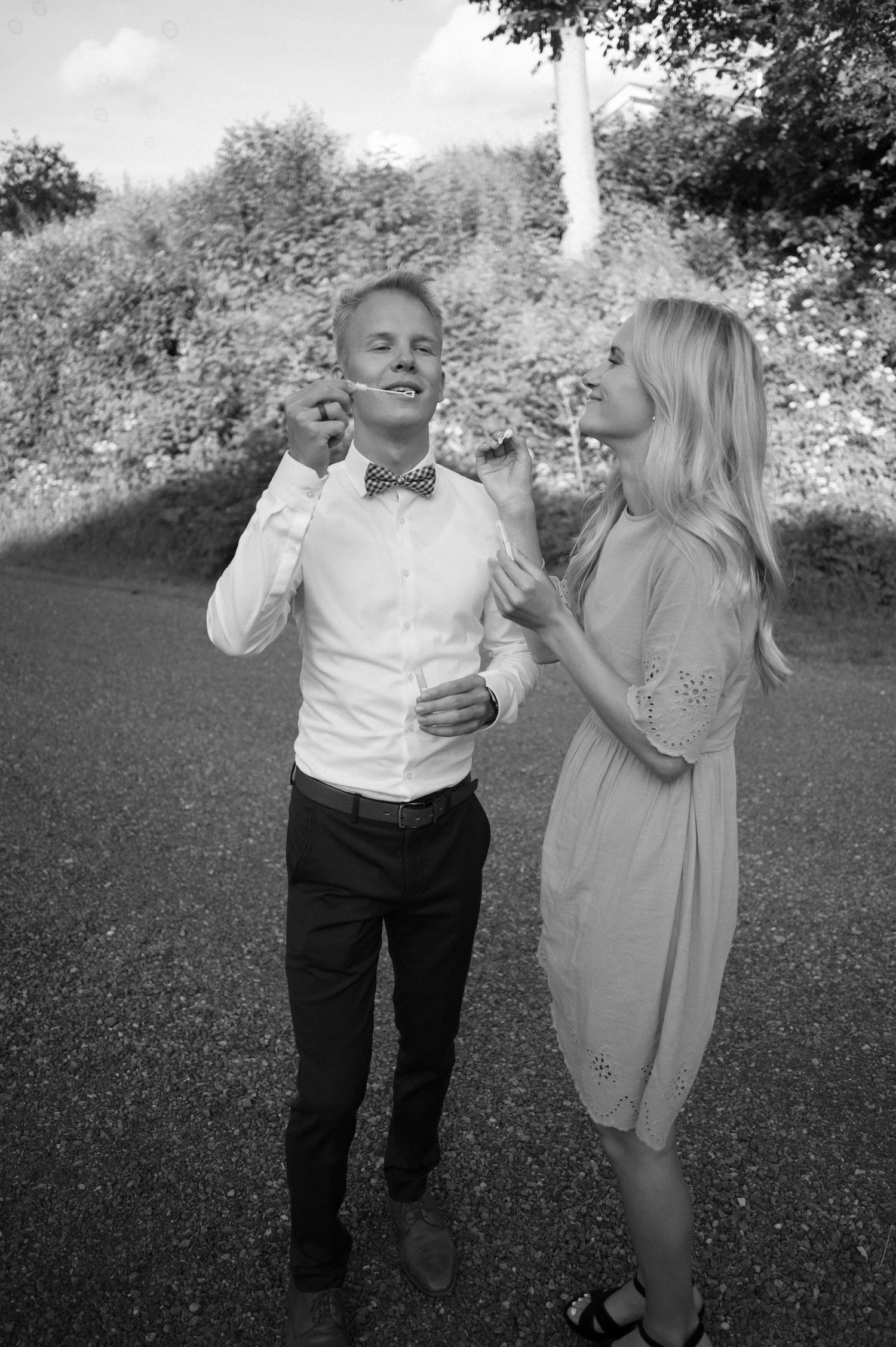 An elderly couple dances and laughs together outdoors in a garden setting.