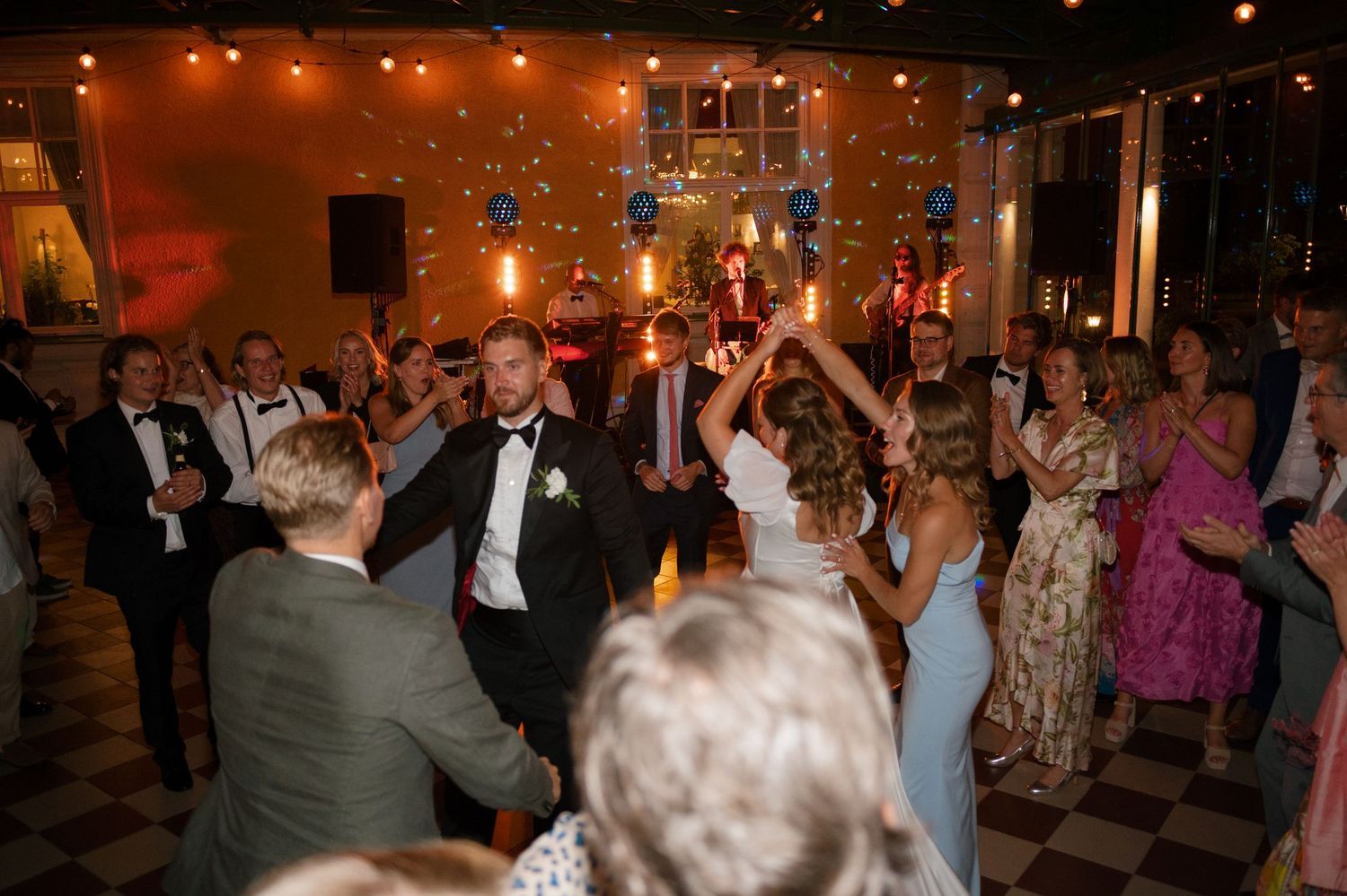 Wedding reception dance party with guests celebrating under warm lighting.