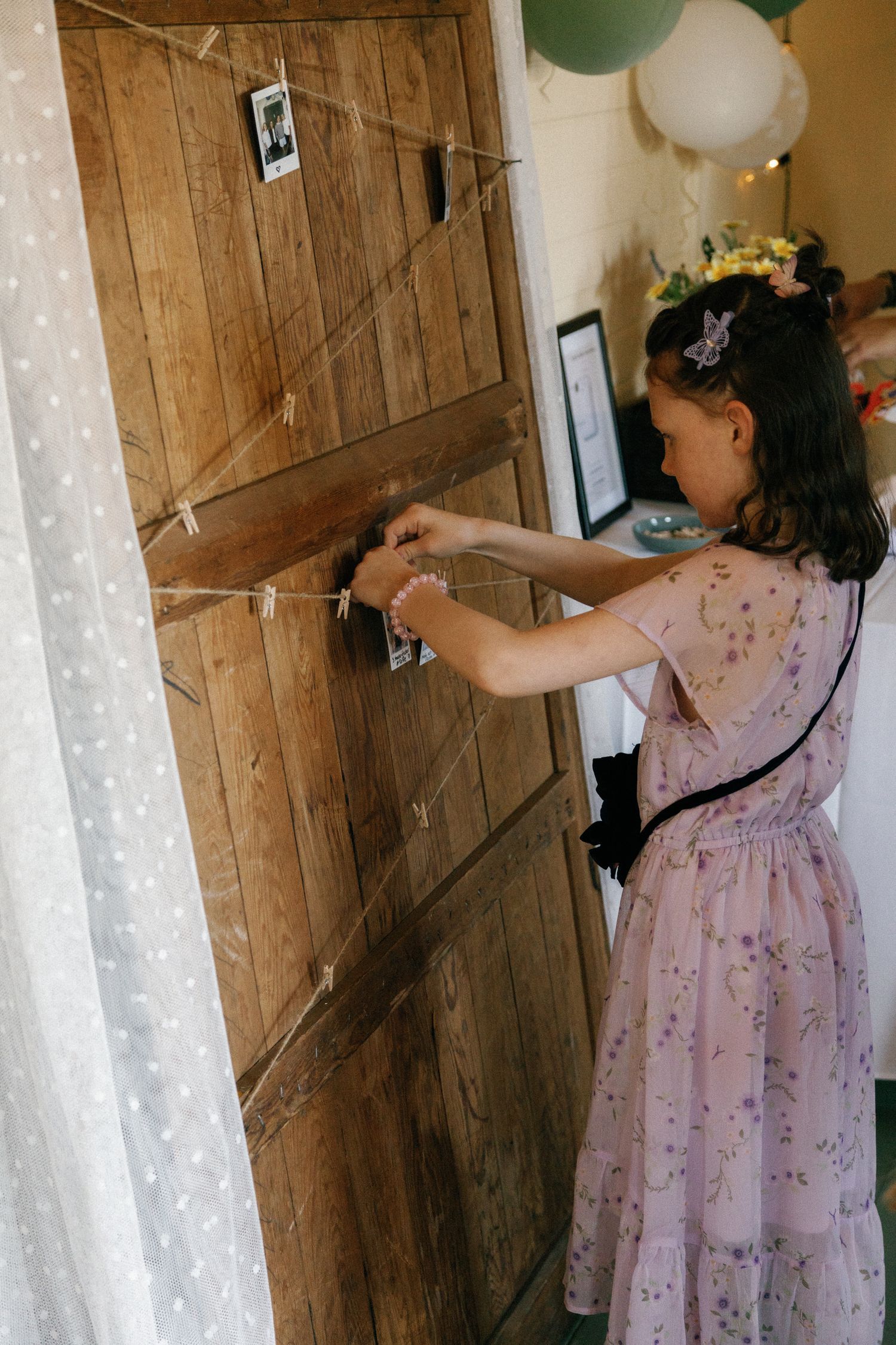 A woman in a floral dress unlocks an old wooden door decorated with balloons.