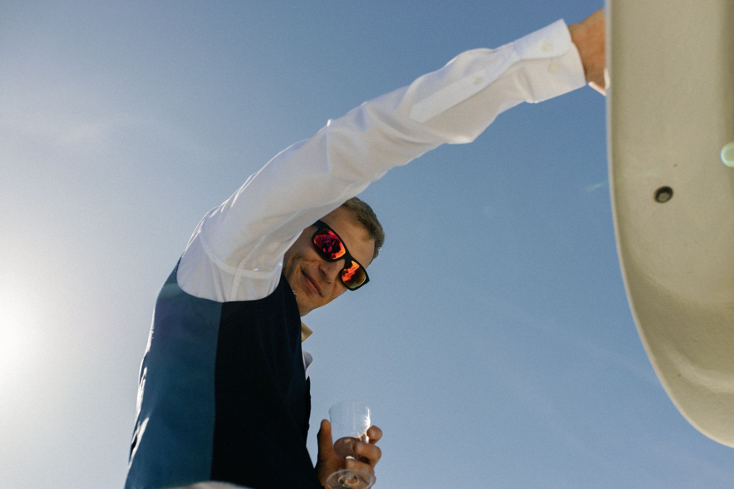 Person in sunglasses and white shirt poses against bright blue sky on boat.