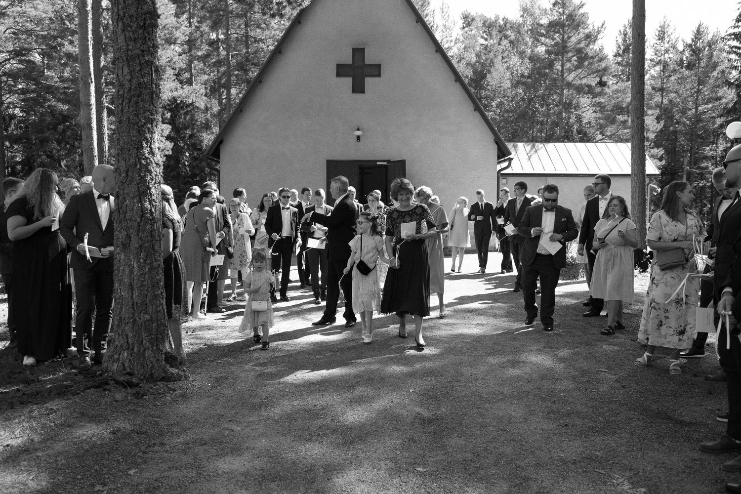 Wedding ceremony takes place outside a charming forest chapel surrounded by pine trees.