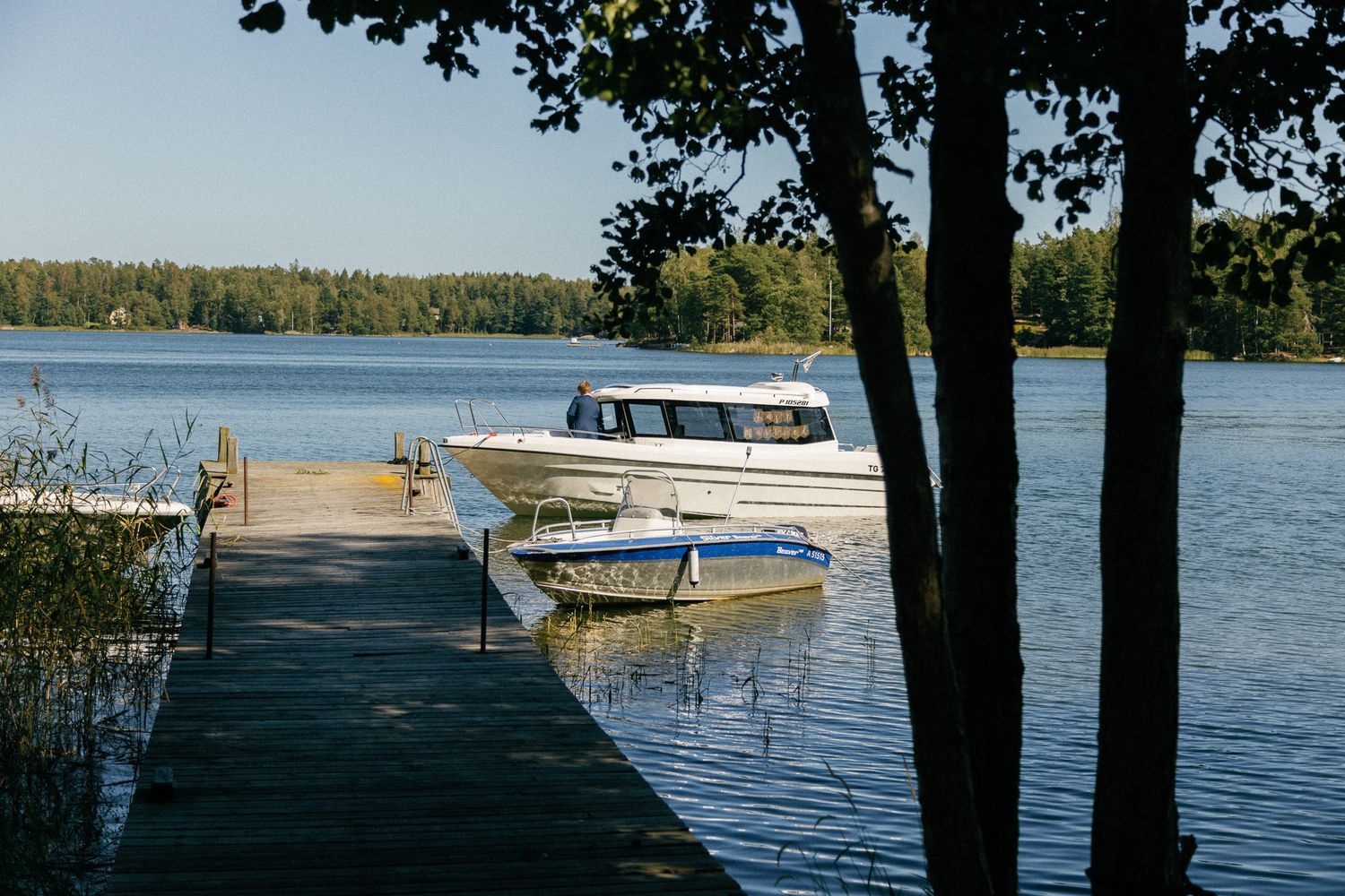 A white boat docked at a wooden pier on a tranquil lake surrounded by trees.