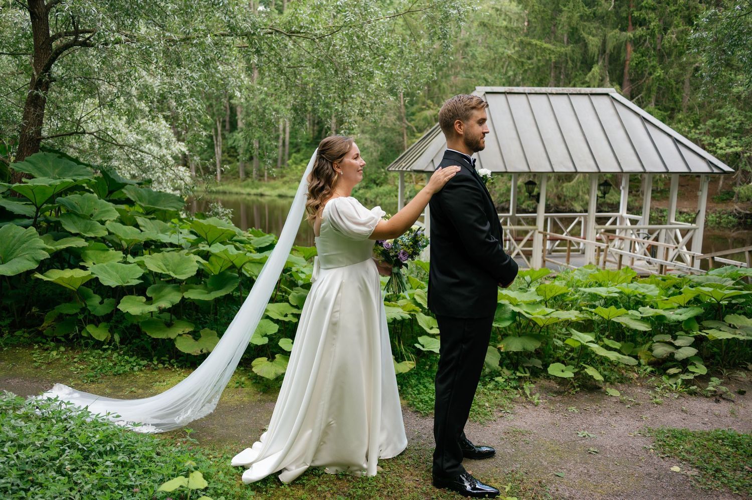 A romantic wedding moment captured in front of a rustic gazebo surrounded by lush garden foliage.