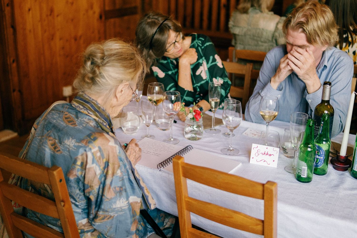 Reception guests seated at long wooden tables with drinks and table settings.