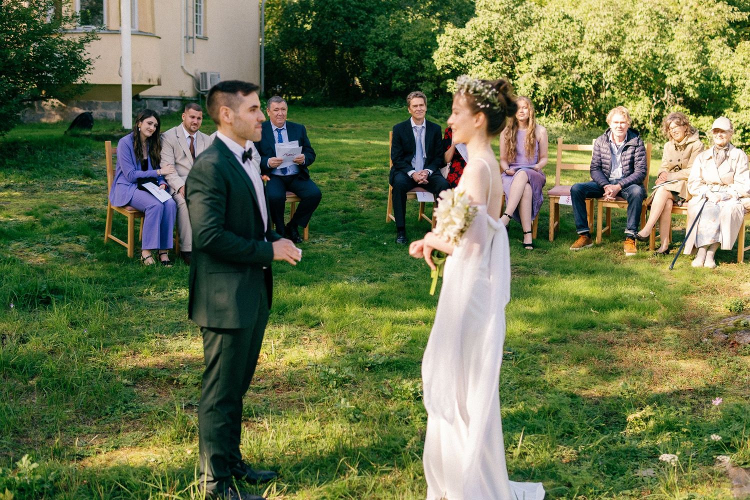 A couple exchanges vows during an intimate outdoor garden wedding ceremony while guests look on from chairs on the lawn.