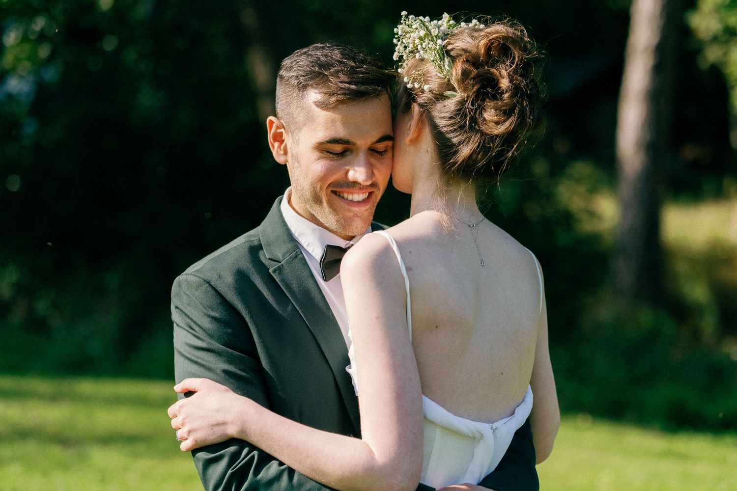 A joyful wedding couple shares a laugh while embracing in a sunny garden setting.