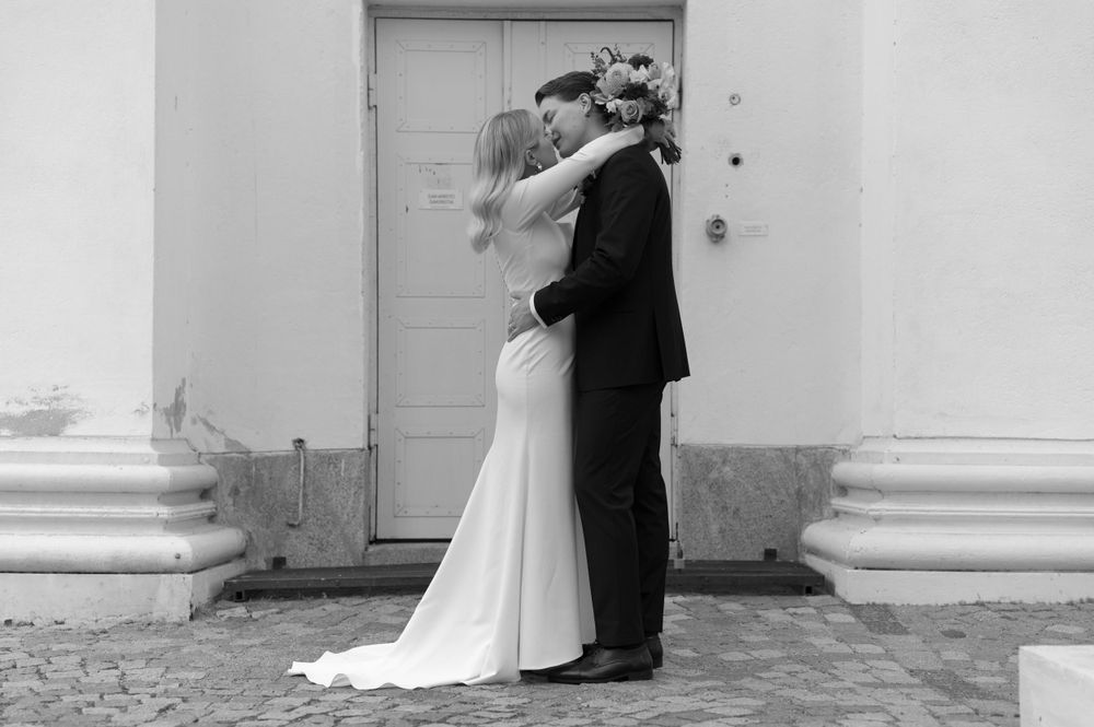 A black and white wedding photo of a couple embracing in front of a white door with classical columns.
