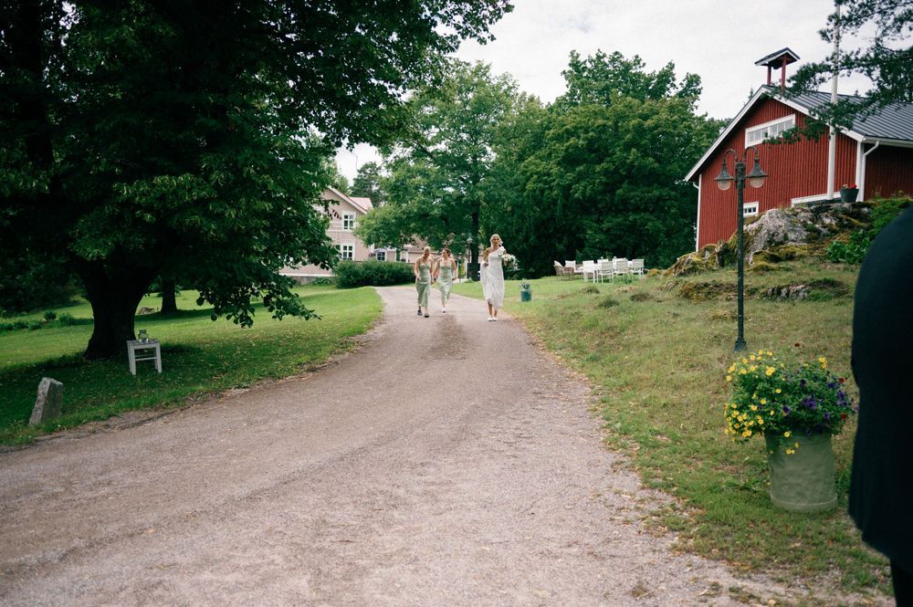 Rural wedding venue setting with dirt path and red buildings surrounded by trees.