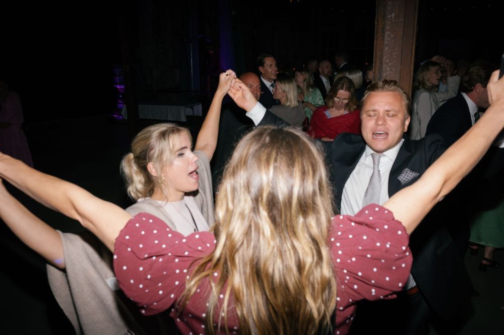Party guests dance enthusiastically with raised arms at a wedding celebration.