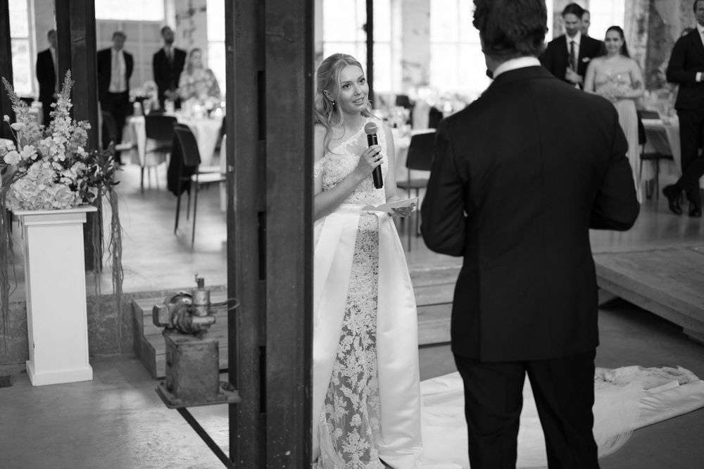 A wedding party stands in an elegant indoor venue with decorative columns and formal attire.