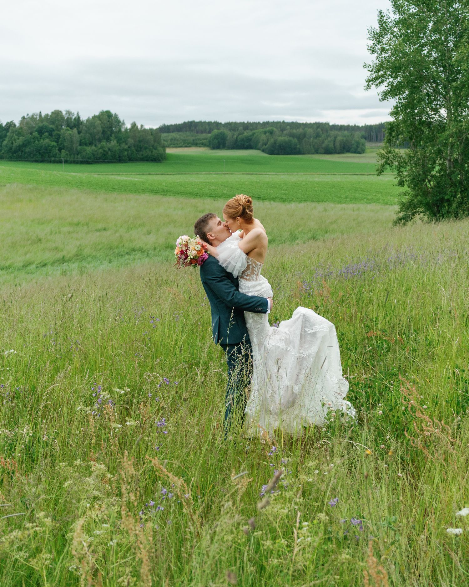 Newlyweds share intimate moments in a summer meadow with wildflowers.