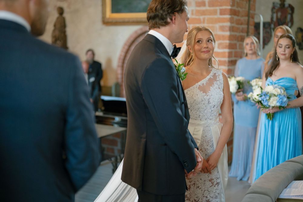 A couple exchanges vows at the altar while bridesmaids in blue dresses look on.
