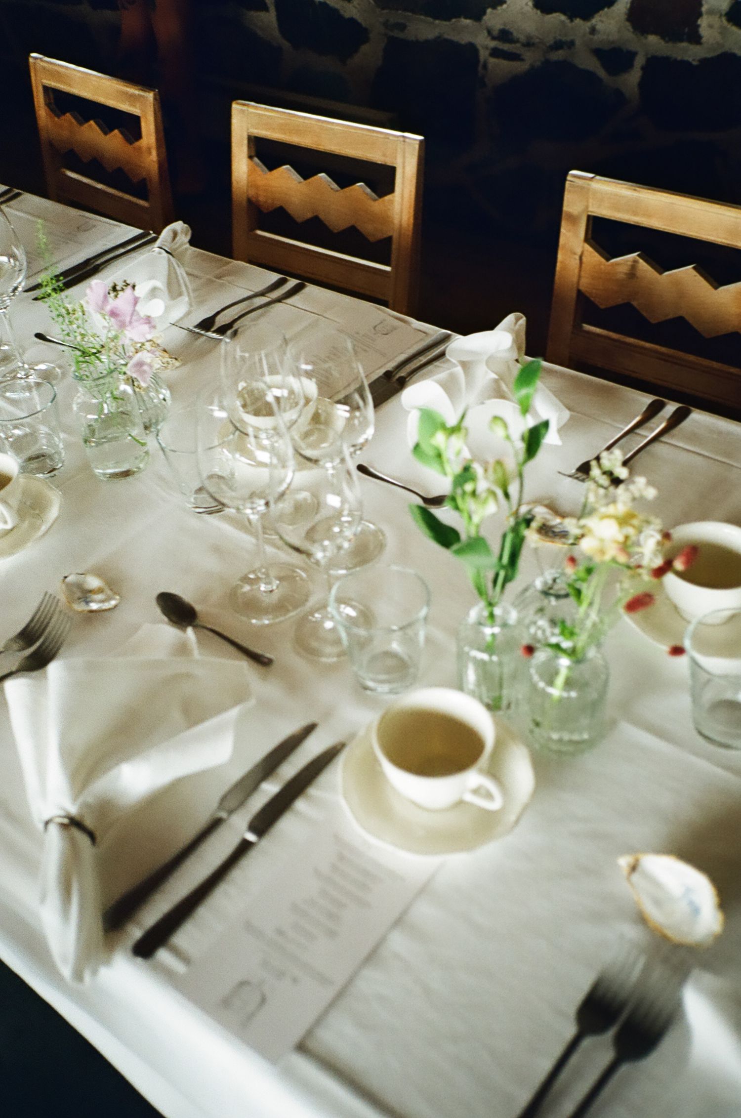 Elegant wedding reception table set with crystal wine glasses, white linens, fresh flowers, and silverware in a rustic venue.