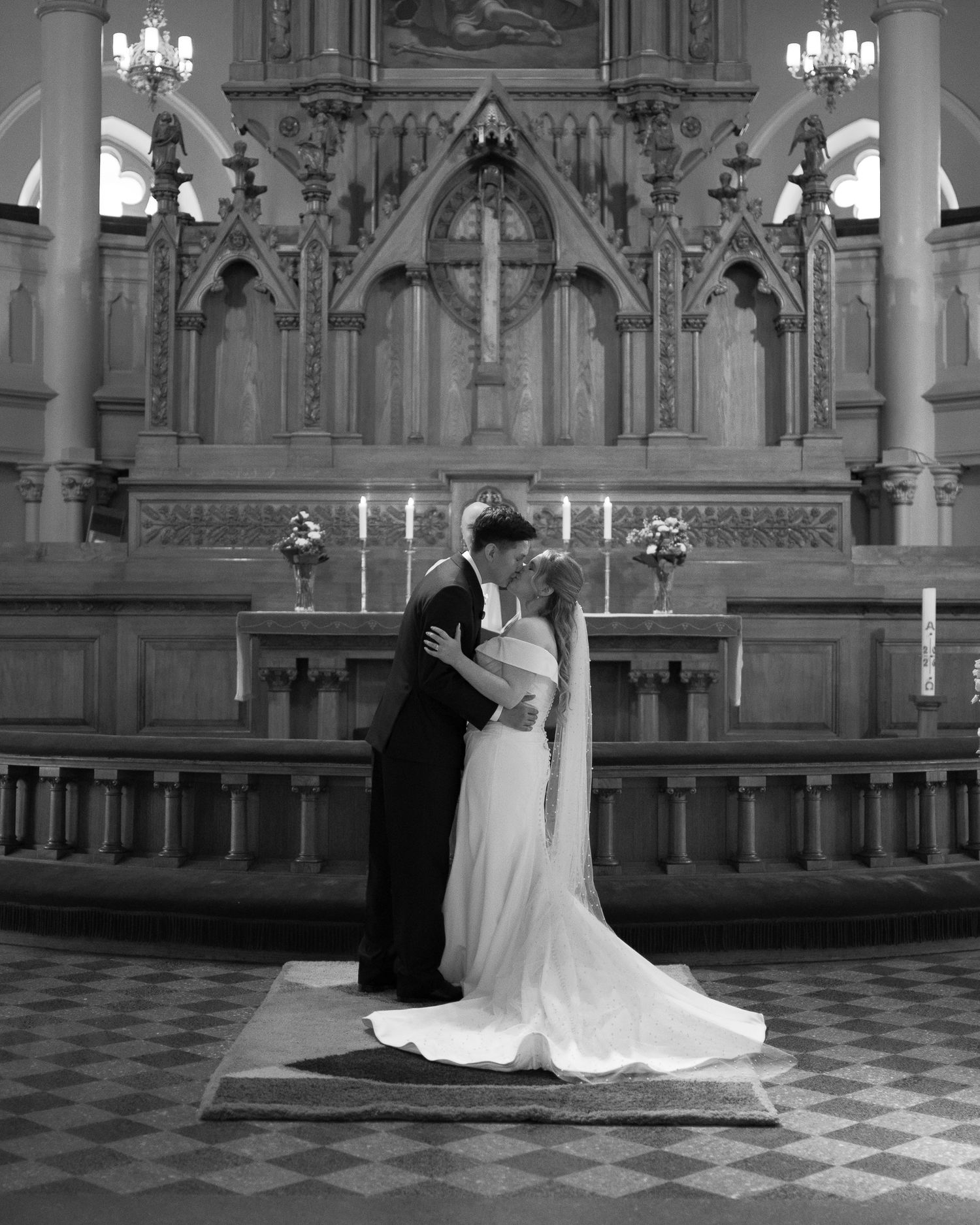 Black and white photo of a bride and groom sharing a kiss at the altar of an ornate church.