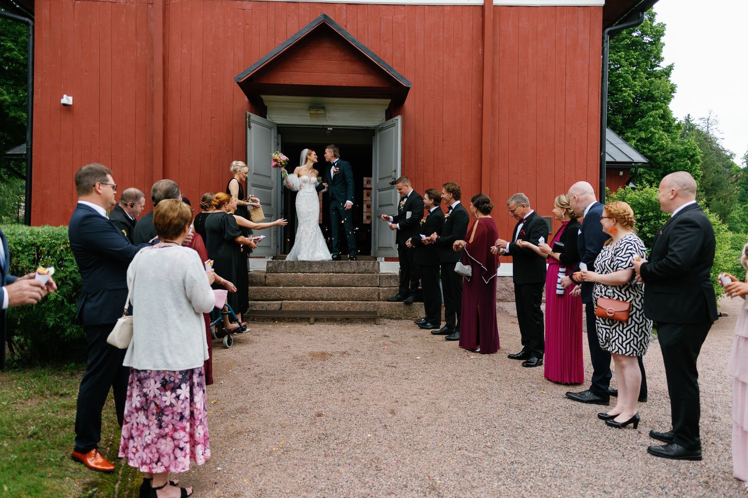 Wedding celebration outside red church with guests forming receiving line.
