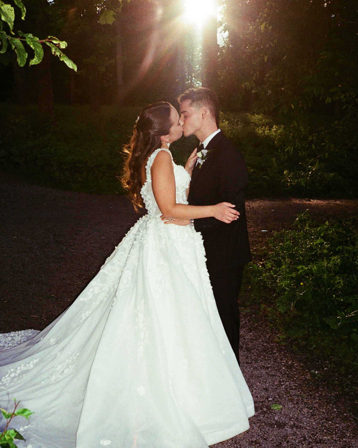 Sunlit wedding portrait with flowing white dress in a garden setting.
