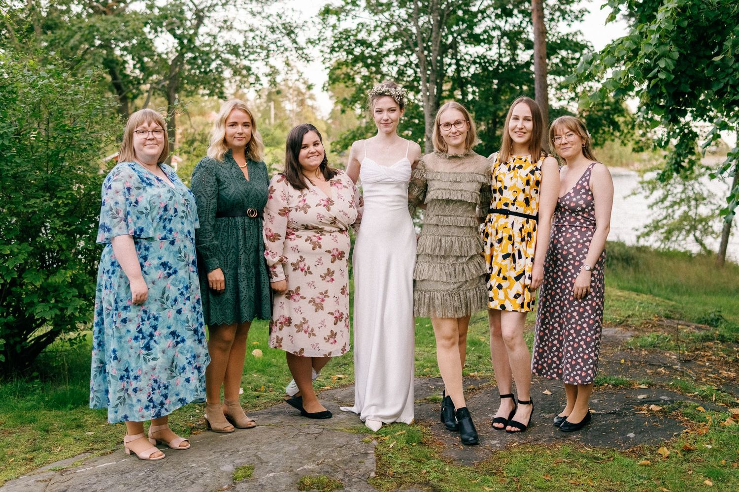 Group photo of bridesmaids in colorful floral dresses standing with the bride outdoors.