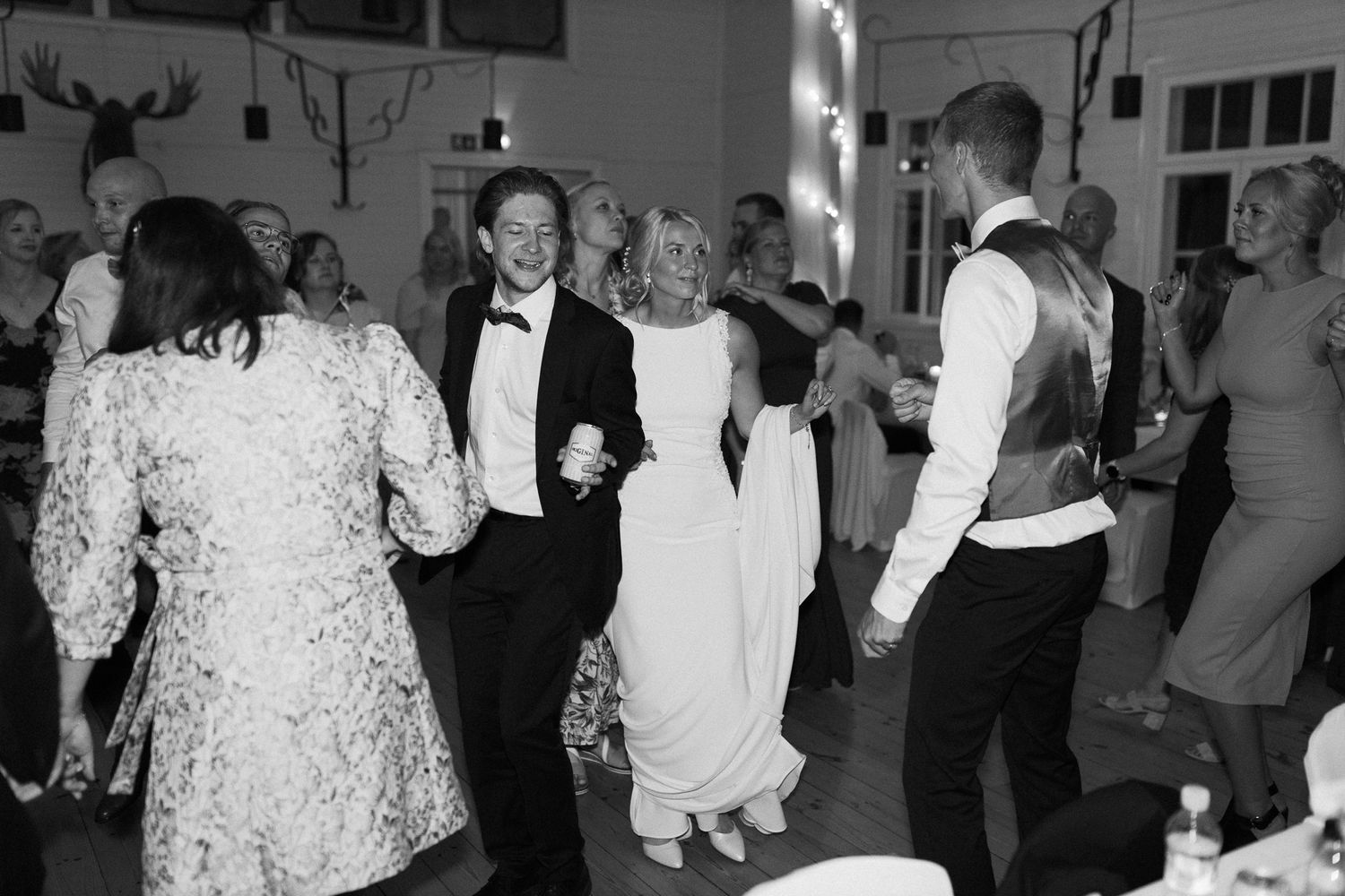 Black and white photo of wedding guests dancing and celebrating in a reception hall.