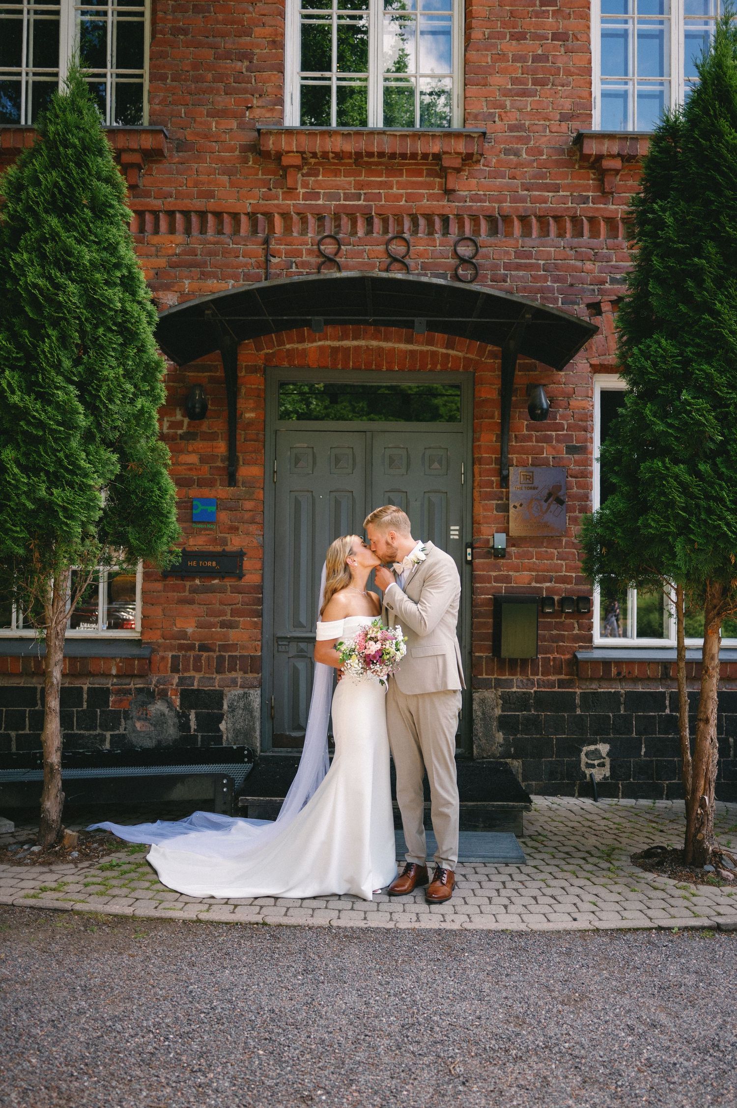 Classic red brick building facade with arched doorway and evergreen landscaping.