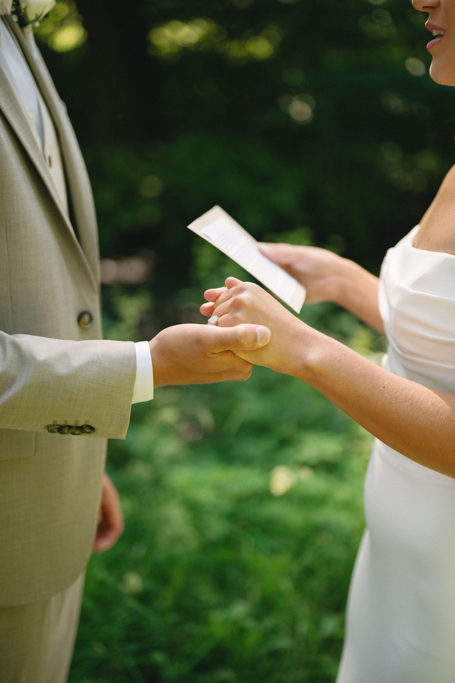 Close-up shot of hands holding wedding vows or letters during an outdoor ceremony.